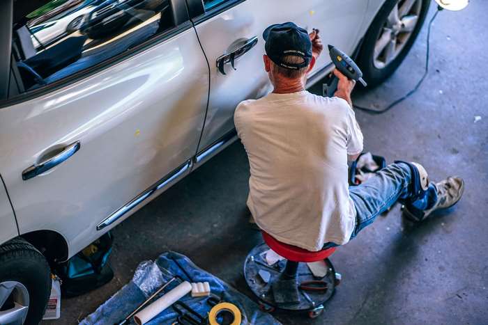Man repairing a car door with a glue gun in a garage