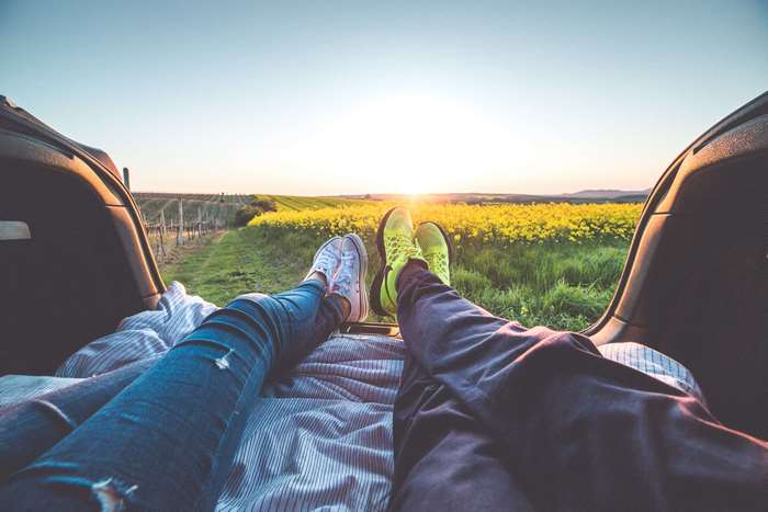 Couple relaxing in car trunk at sunset in flower field