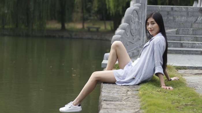 Young Asian woman sitting by a pond on a stone bridge