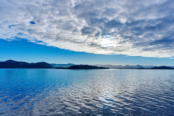 Calm Sea and Mountains Under Cloudy Sky