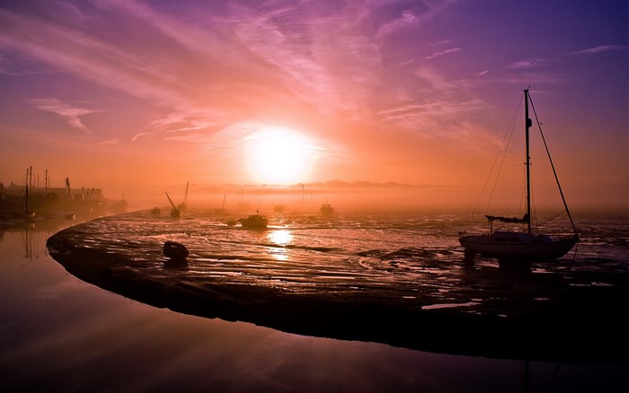 Boats on a foggy shore at sunset