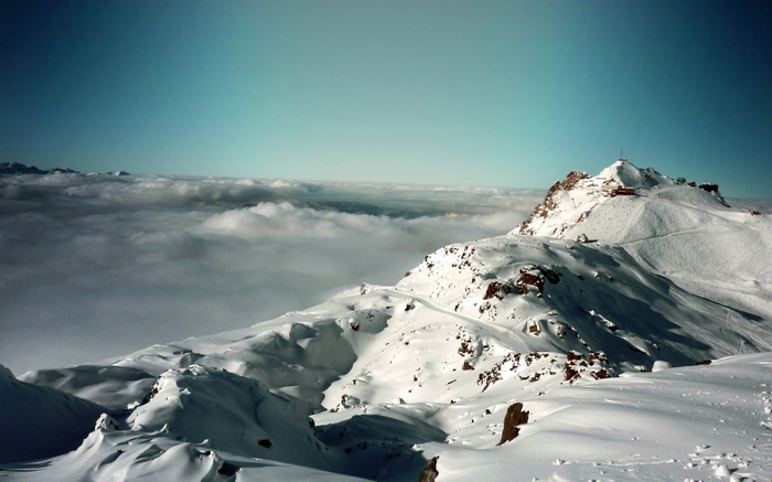 Snowy mountain peak with buildings and clouds below