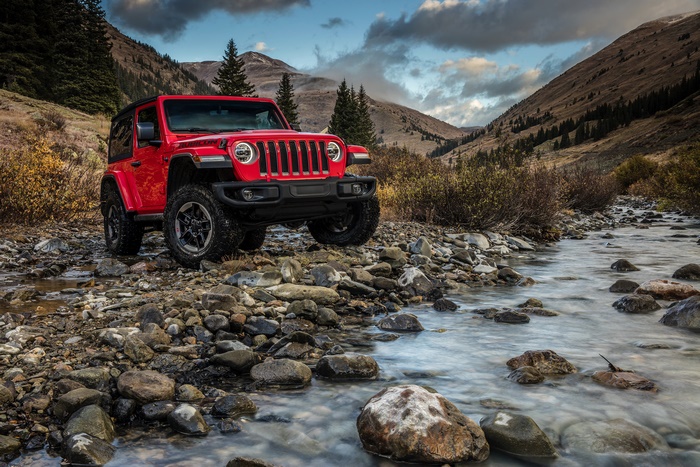 Red Jeep Wrangler parked by a stream in a mountain valley