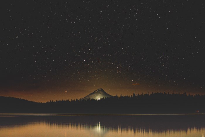 Starry night sky over a lake and forest with a mountain
