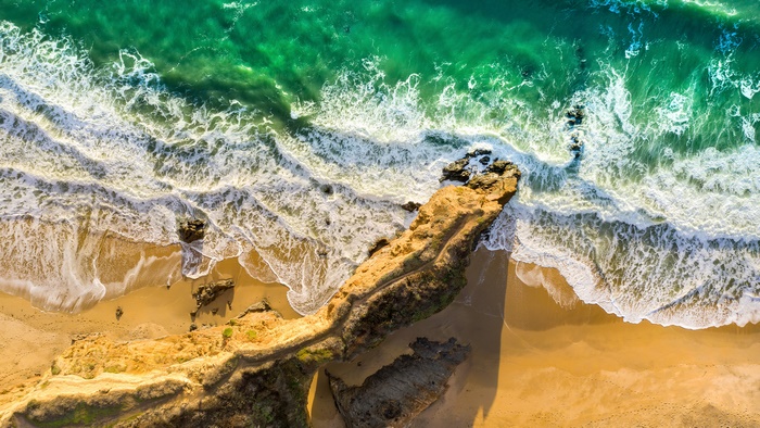 Aerial view of a rocky coastline with green ocean waves