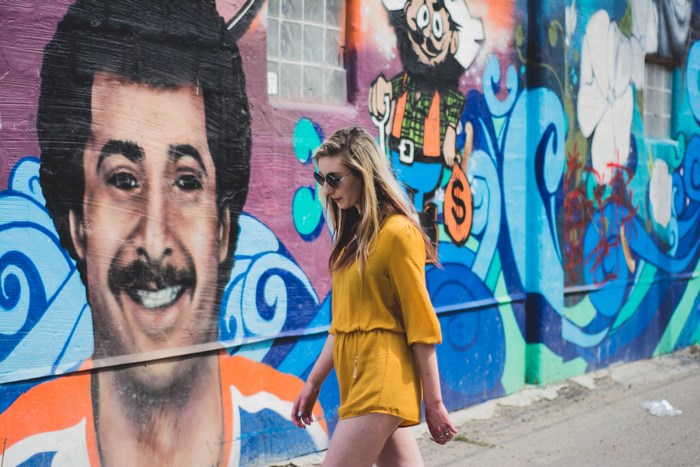 Woman walking past a mural of a man and cartoon character