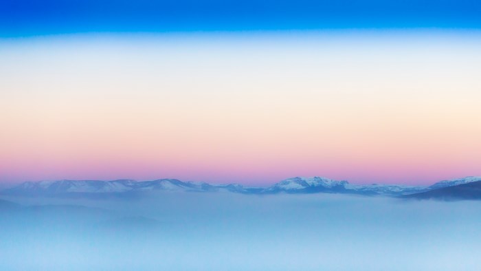 Snowy mountains above clouds at sunrise or sunset