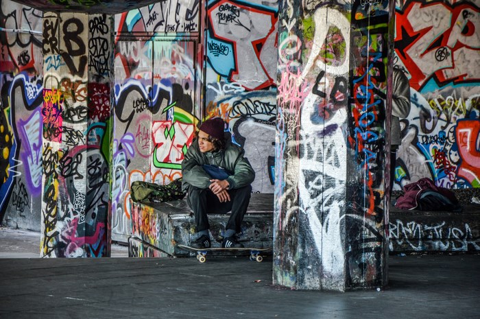 Skateboarder sitting in graffiti-covered urban area