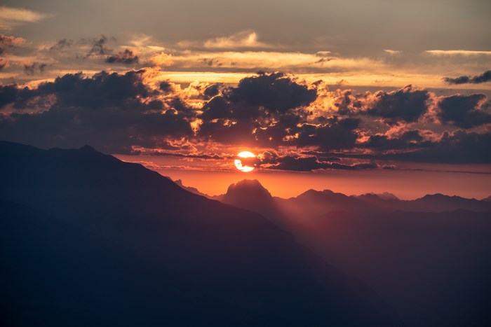 Sunset over mountains with sunrays and clouds