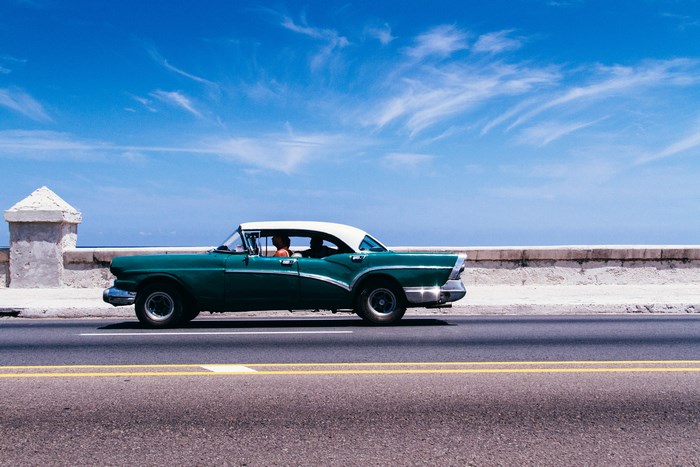 Green vintage American car driving on a road in Cuba