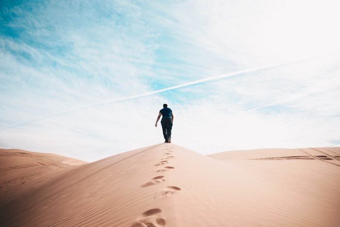 Person walking on sand dune under blue sky
