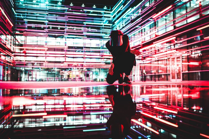 Person crouching in front of neon lights reflection