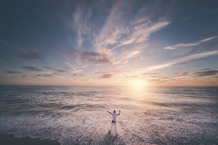 Man with arms raised in ocean at sunset