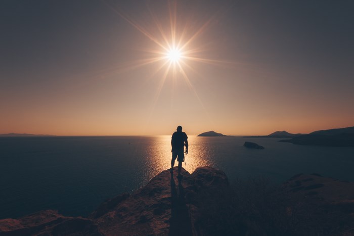 Silhouette of a person on a cliff overlooking the ocean at sunset