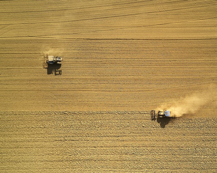Tractors plowing a dry field from above