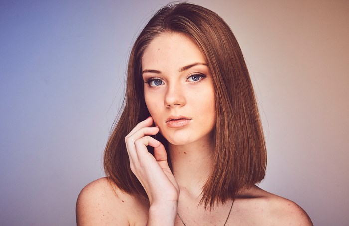Woman with brown hair and blue eyes, hand on face