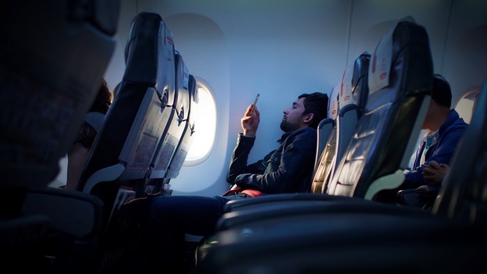 Man on airplane using phone by window