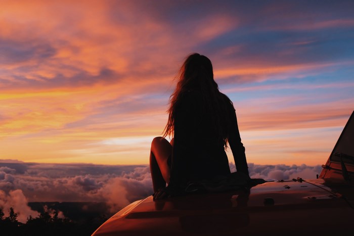 Woman sitting on a jeep overlooking clouds at sunset