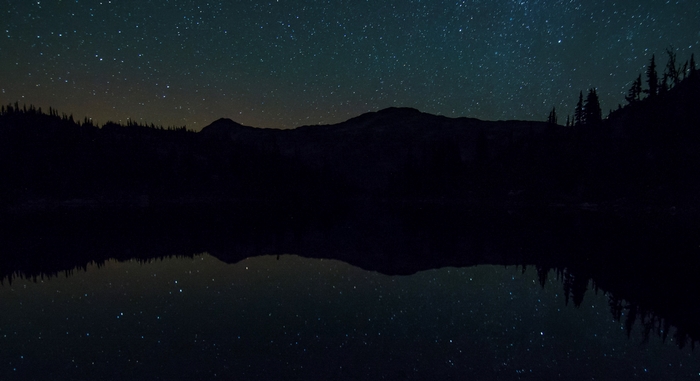 Night sky over mountains and lake reflection