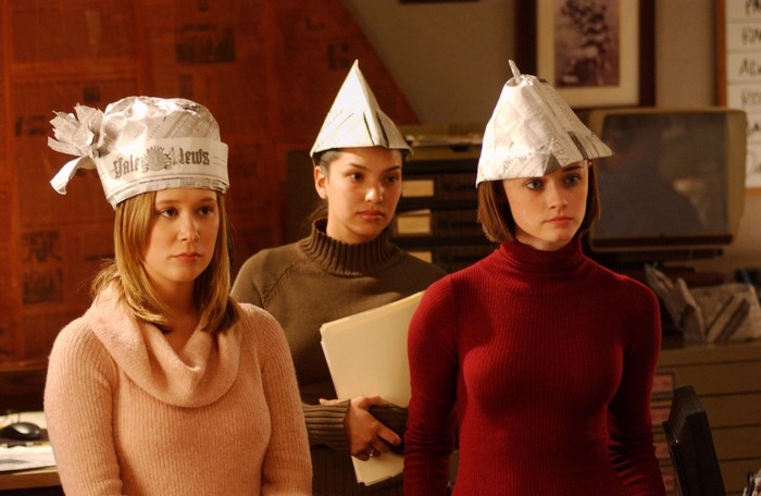 Three young women wearing newspaper hats