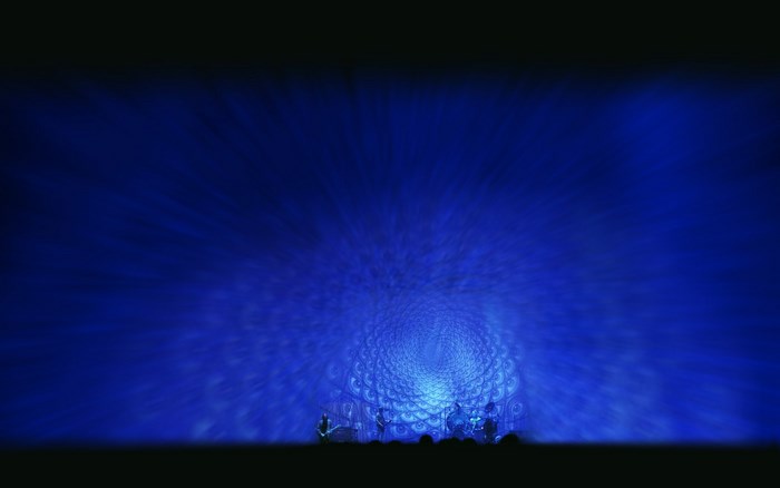 Band performing on stage with blue psychedelic background