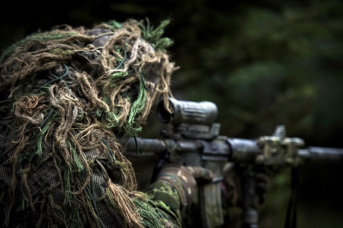 Sniper in ghillie suit aiming rifle