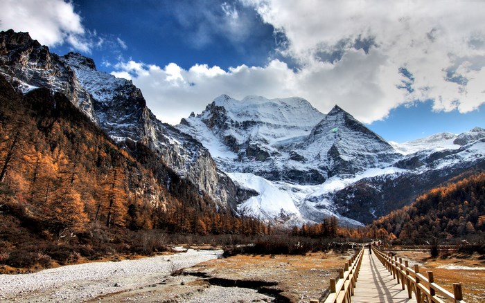Snow-capped mountains and autumn trees with a wooden bridge