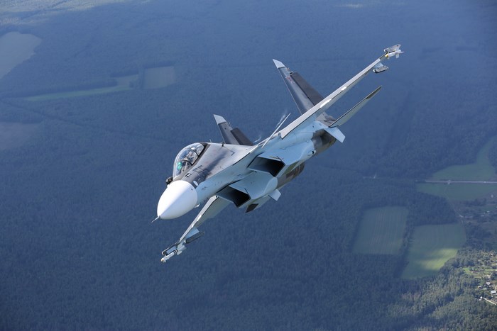 Sukhoi Su-30 fighter jet in flight over forest
