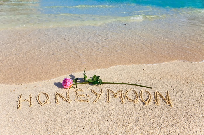 Honeymoon written in sand with a rose on a beach
