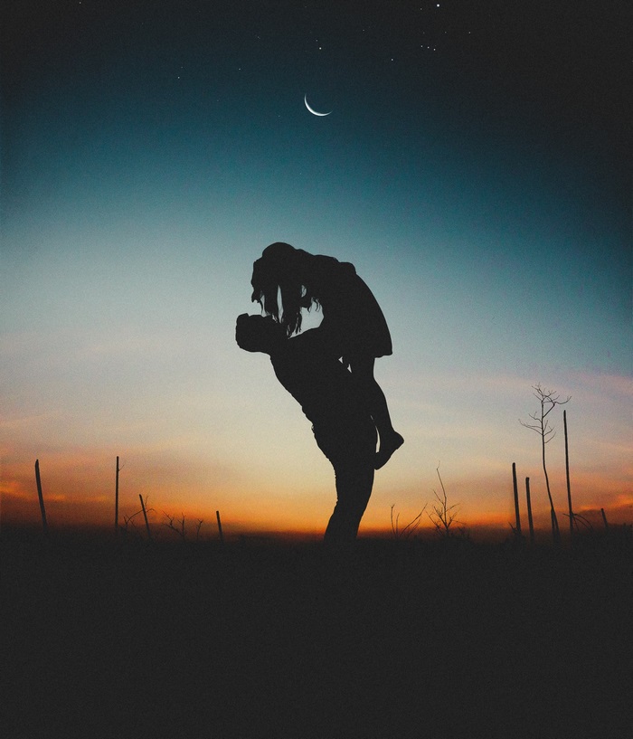 Couple silhouetted against sunset and moonlit sky