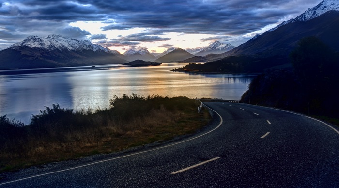 Road curving towards snow-capped mountains and lake in New Zealand 4K