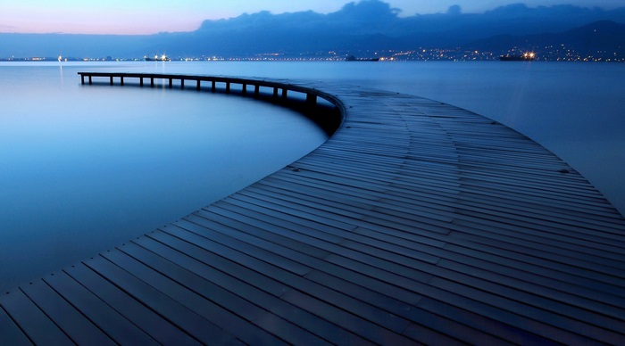 Curved wooden pier on a calm lake at dusk
