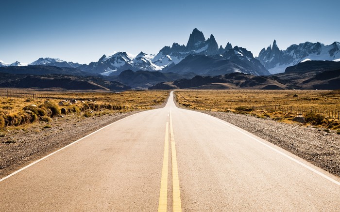 Road leading to snowy mountain peaks under clear sky