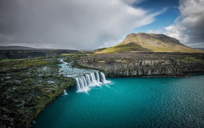 Waterfall flowing into turquoise water with mountain landscape