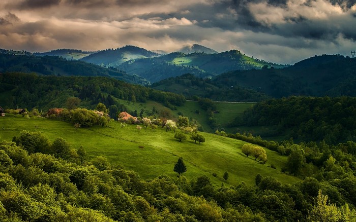 Rolling green hills with scattered houses and trees under cloudy sky
