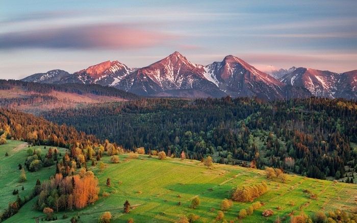 Sunrise over snowy mountains and green fields