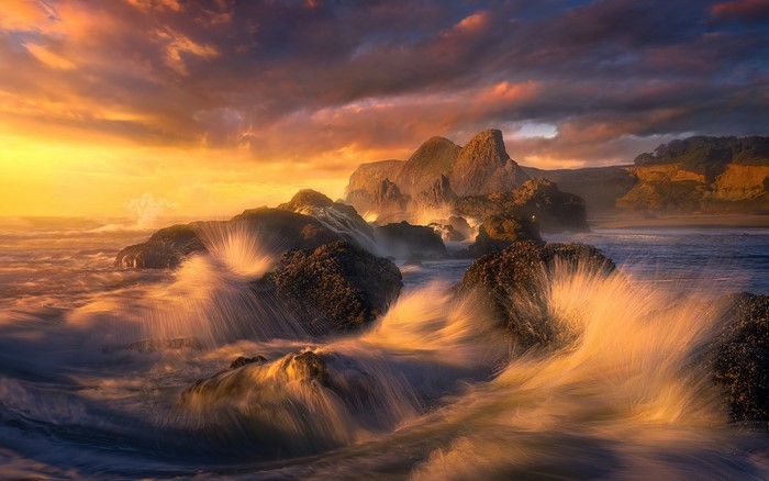 Sunset over rocky coast with waves crashing in Oregon