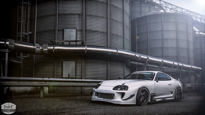 White Toyota Supra parked near industrial silos