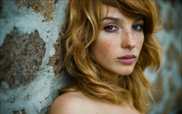 Woman with freckles leaning against a stone wall