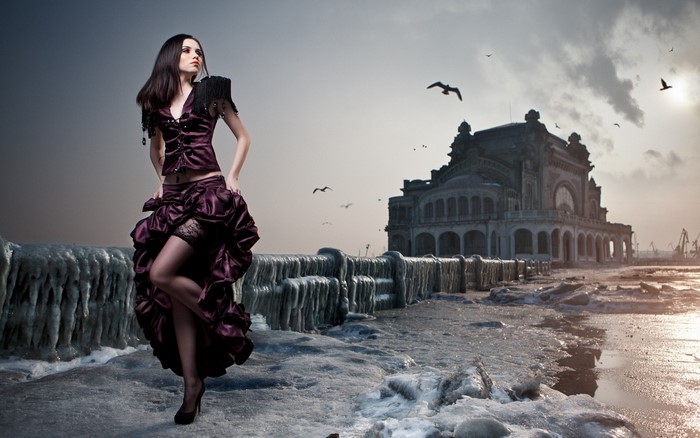 Woman in purple dress on icy shore with old building