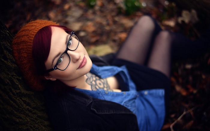 Woman with glasses and tattoos lying down outdoors