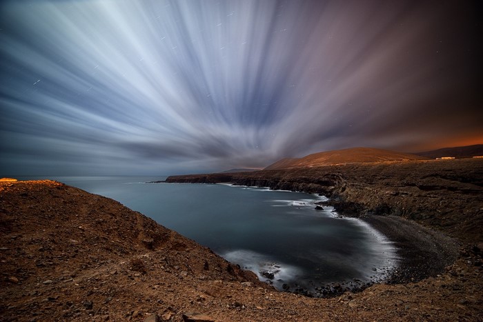 Long exposure of clouds over a rocky coastline at night