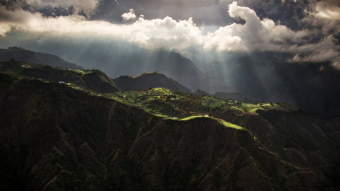 Sun rays breaking through clouds over mountainous landscape