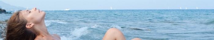 Woman sunbathing on a beach with sailboats in the distance