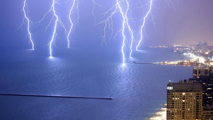 Lightning strikes over a city and sea at night
