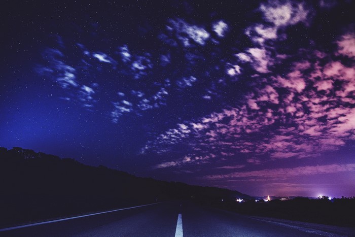 Night road under starry sky with clouds