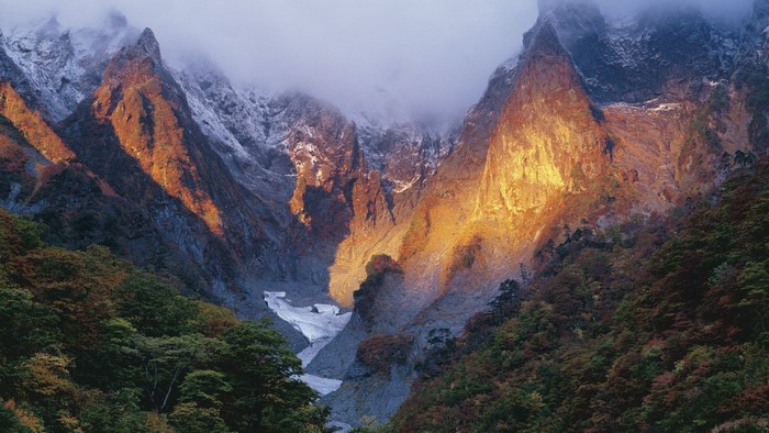 Mountain valley with snow and autumn trees at sunrise