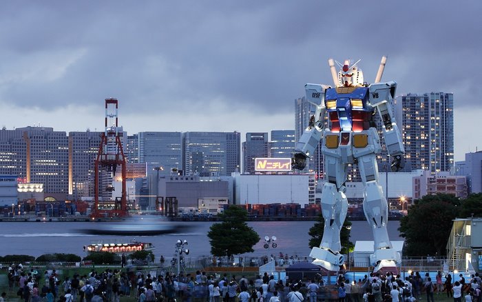 Giant Gundam statue in a city harbor at dusk