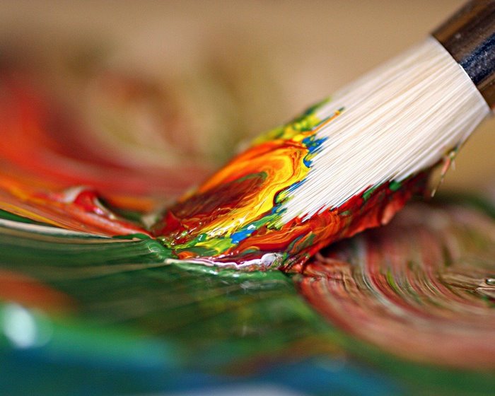Paintbrush mixing colorful paints on a palette