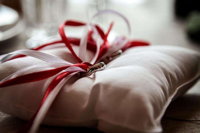 Wedding rings on a pillow with red and white ribbons
